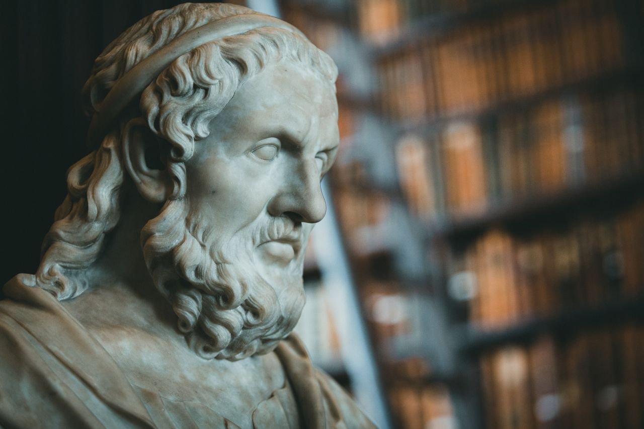 Close-up of a classical marble statue with blurred bookcases in the background.