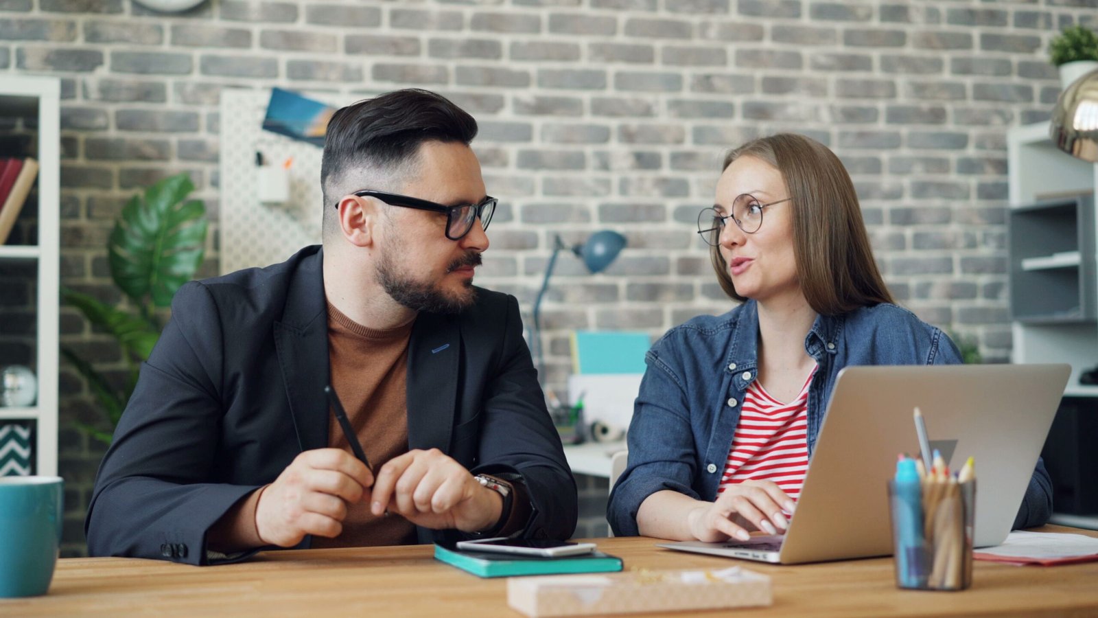 Two colleagues discuss ideas at a desk in a contemporary office, utilizing technology for collaboration.