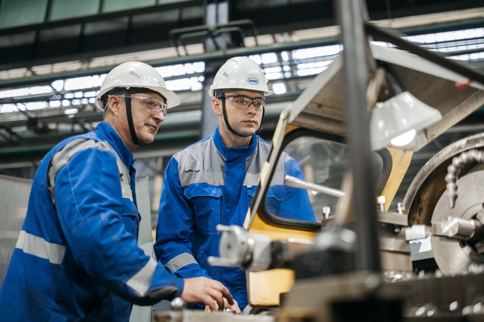 Le feedback positif d'impact : dépasser le simple « bravo » Two industrial workers in protective gear operate machinery in a factory setting.