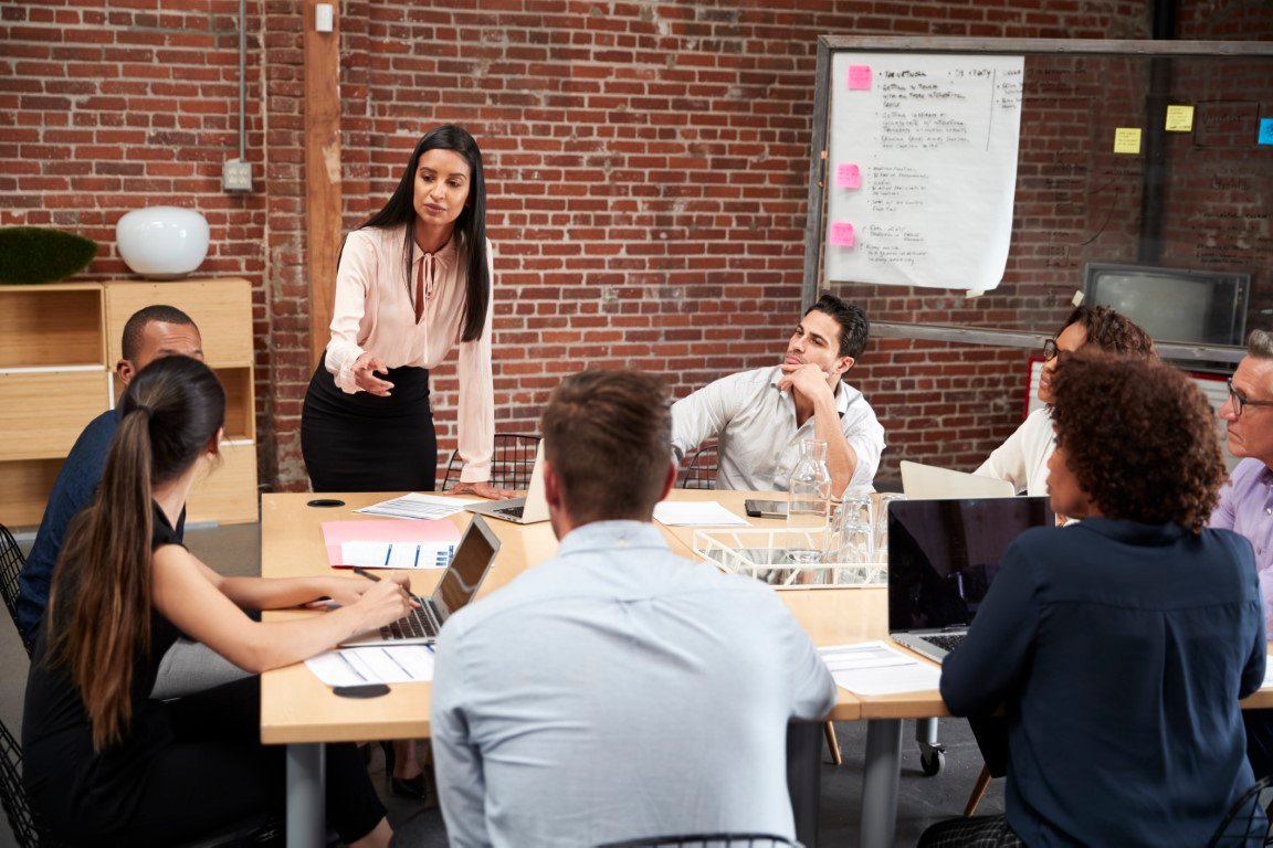 Comment développer une motivation durable? young businesswoman standing and leading office meeting around table