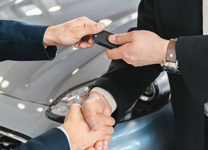 Close-up of a business handshake as car keys are handed over, symbolizing a new car purchase.