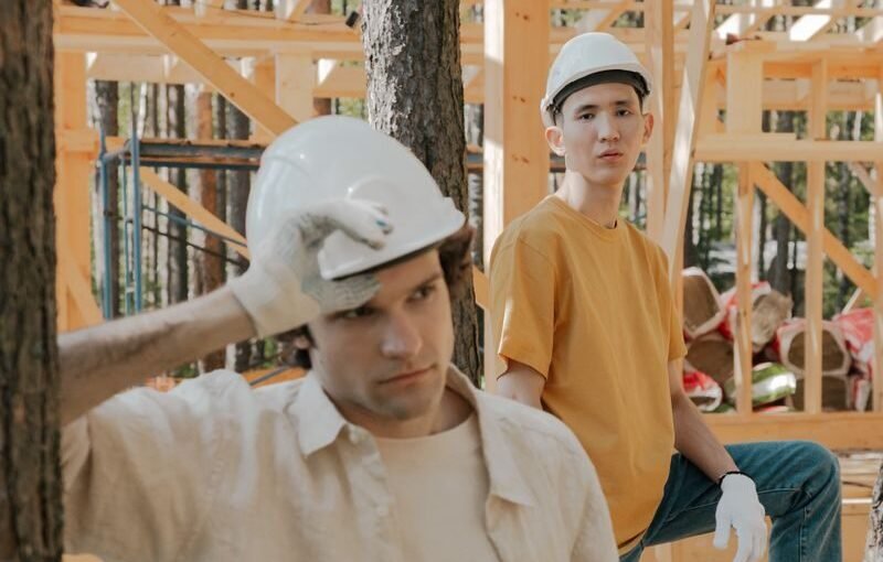 Comment gérer les émotions négatives au travail? Two young men in hard hats at an outdoor wooden construction site.